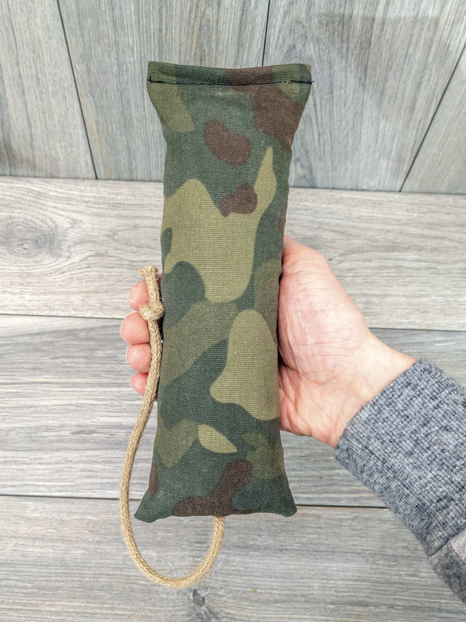 A hand holding a catnip kicker made from a green military camo themed fabric