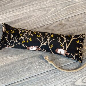 A catnip kicker made from a black fabric that has a pattern showing birds sitting in a tree. 