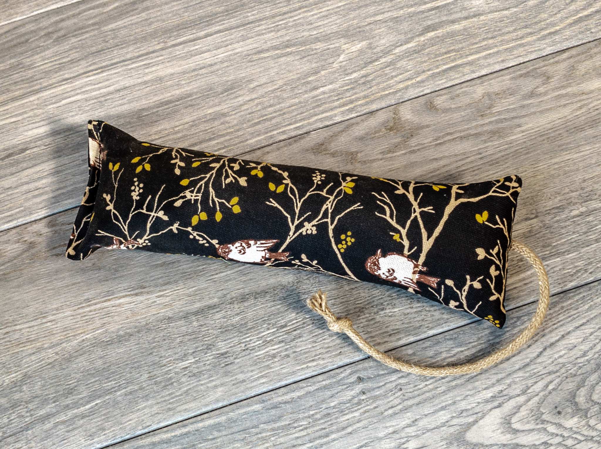 A catnip kicker made from a black fabric that has a pattern showing birds sitting in a tree.