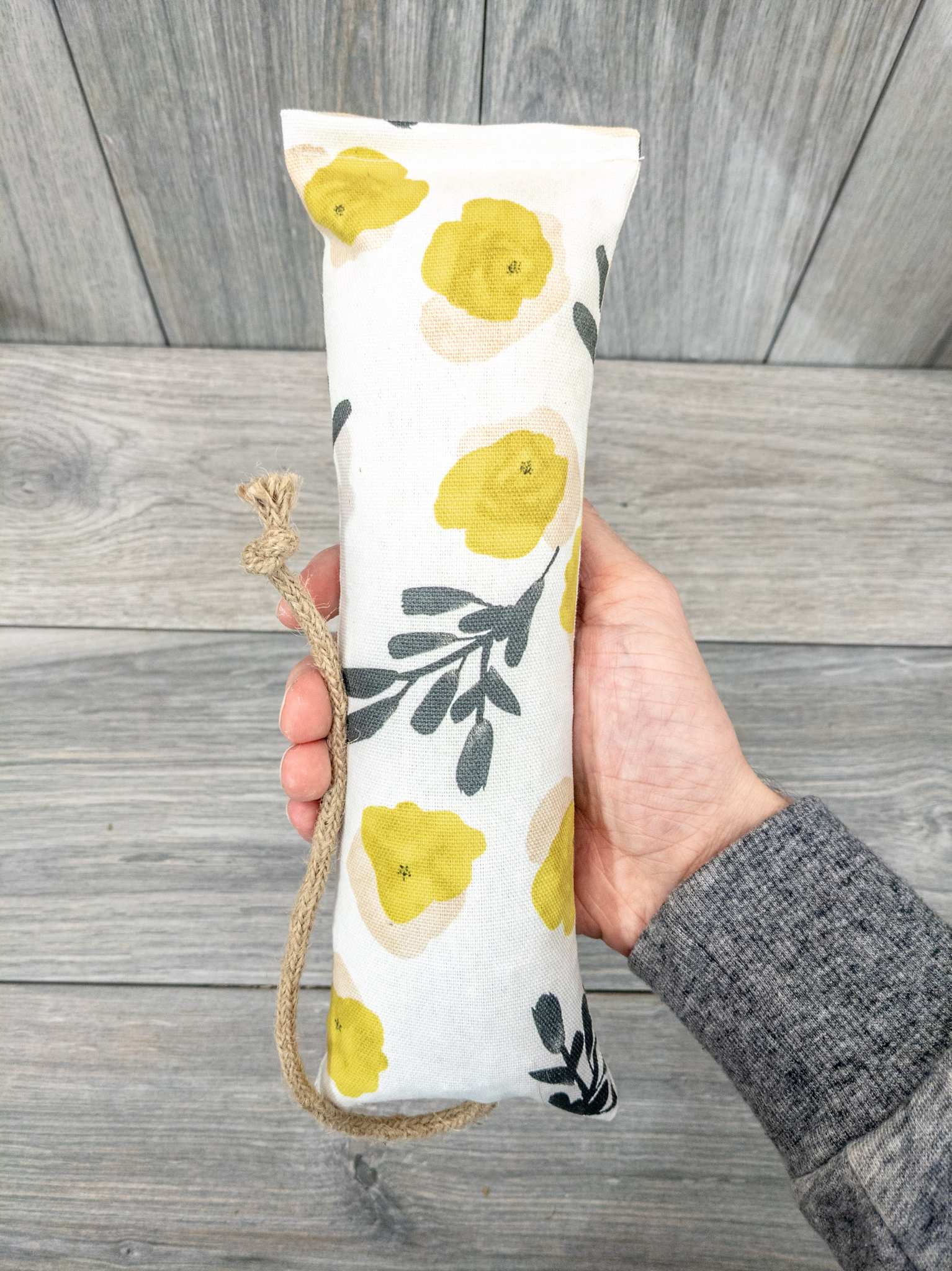 A hand holding a catnip kicker made from a white fabric with yellow flower and green spring of foliage print