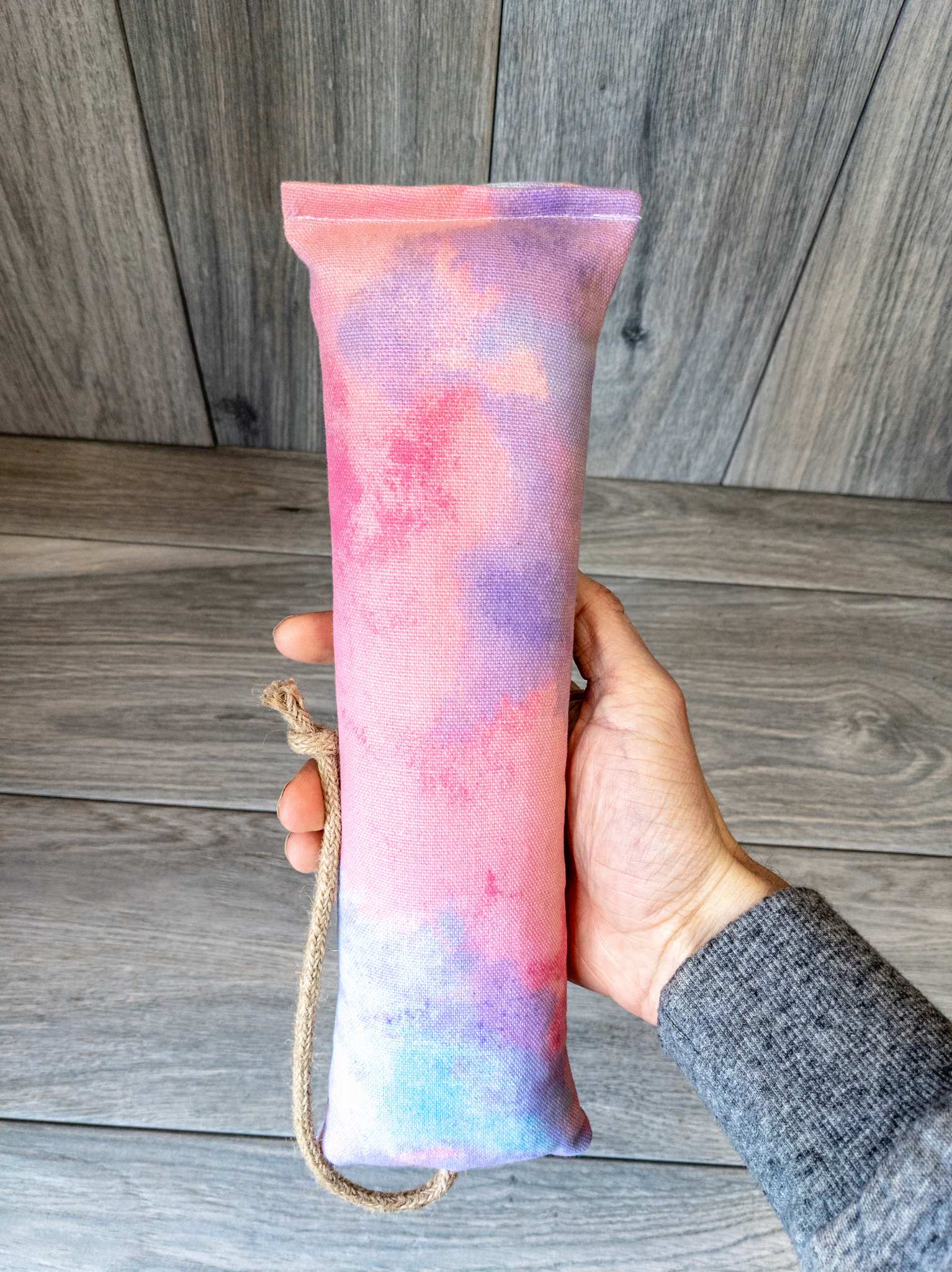 A hand holding a catnip kicker made from a fabric that looks like multicolor pink, blue, and orange cotton candy