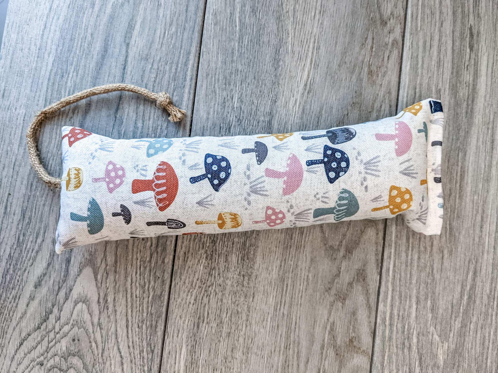 A catnip kicker made from a white fabric with various mushrooms printed o nit.