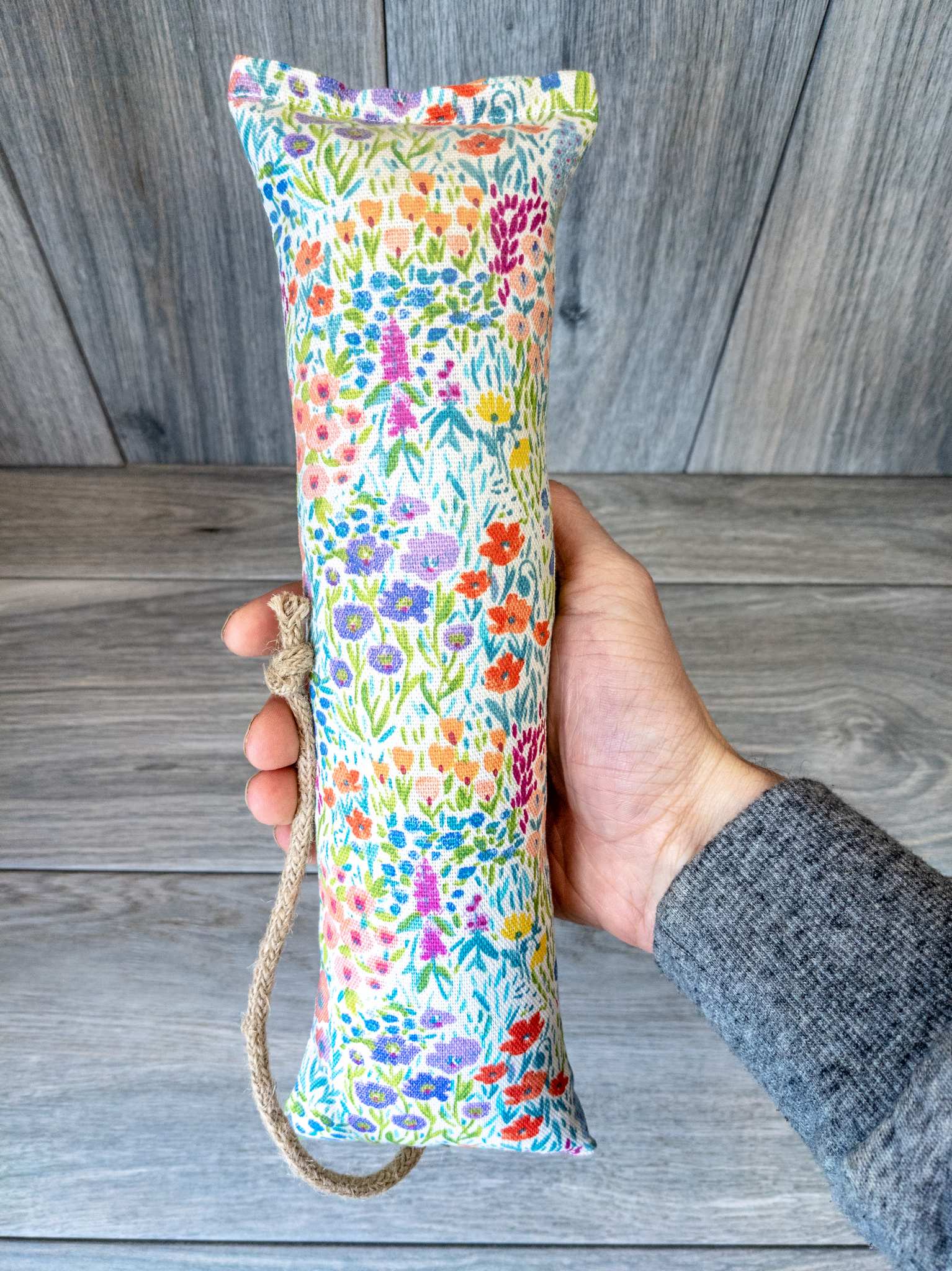A hand holding a catnip kicker made from a white multicolor watercolor wildflower print