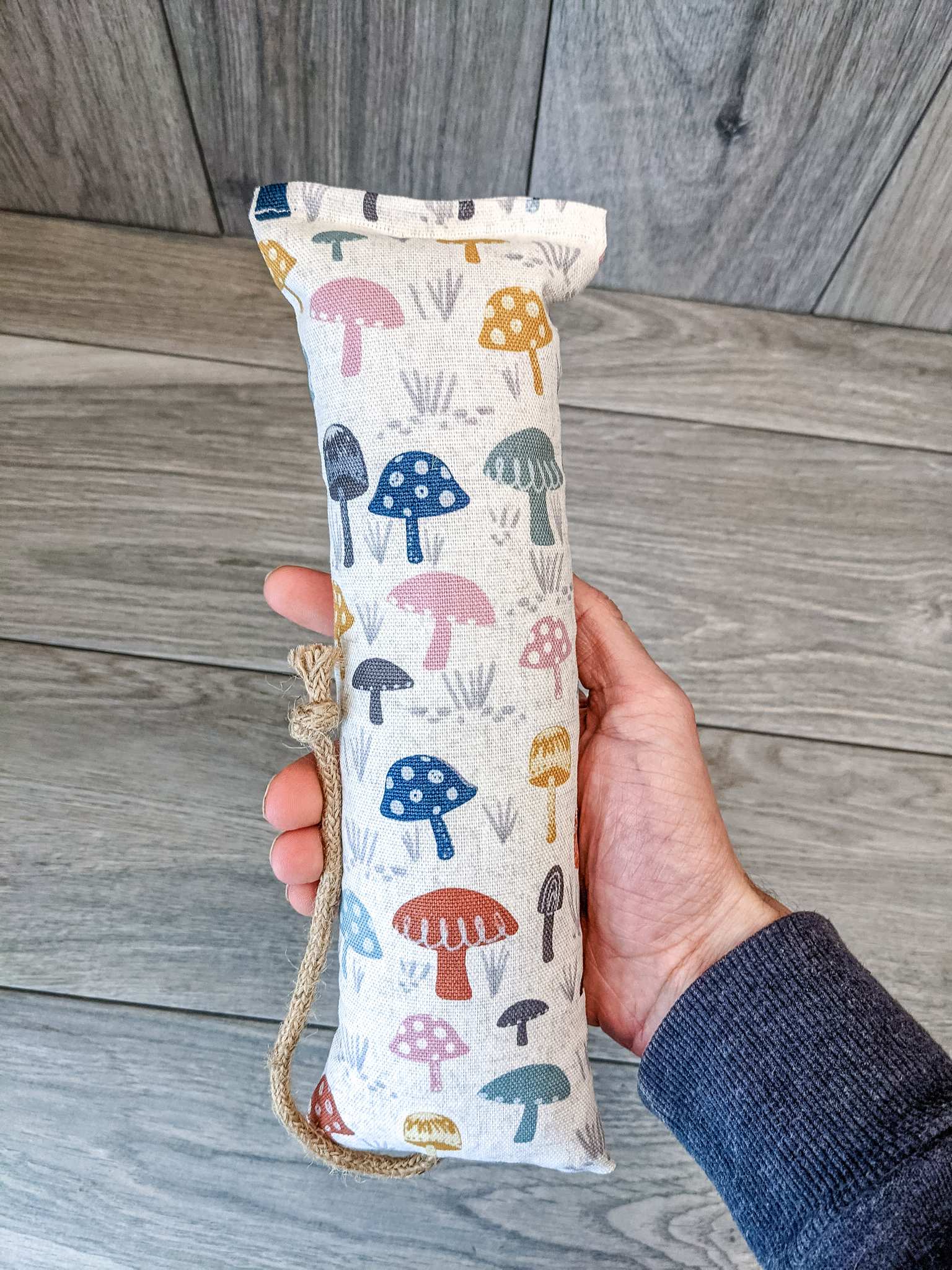 A hand holding a catnip kicker made from a white fabric with various mushrooms printed o nit.
