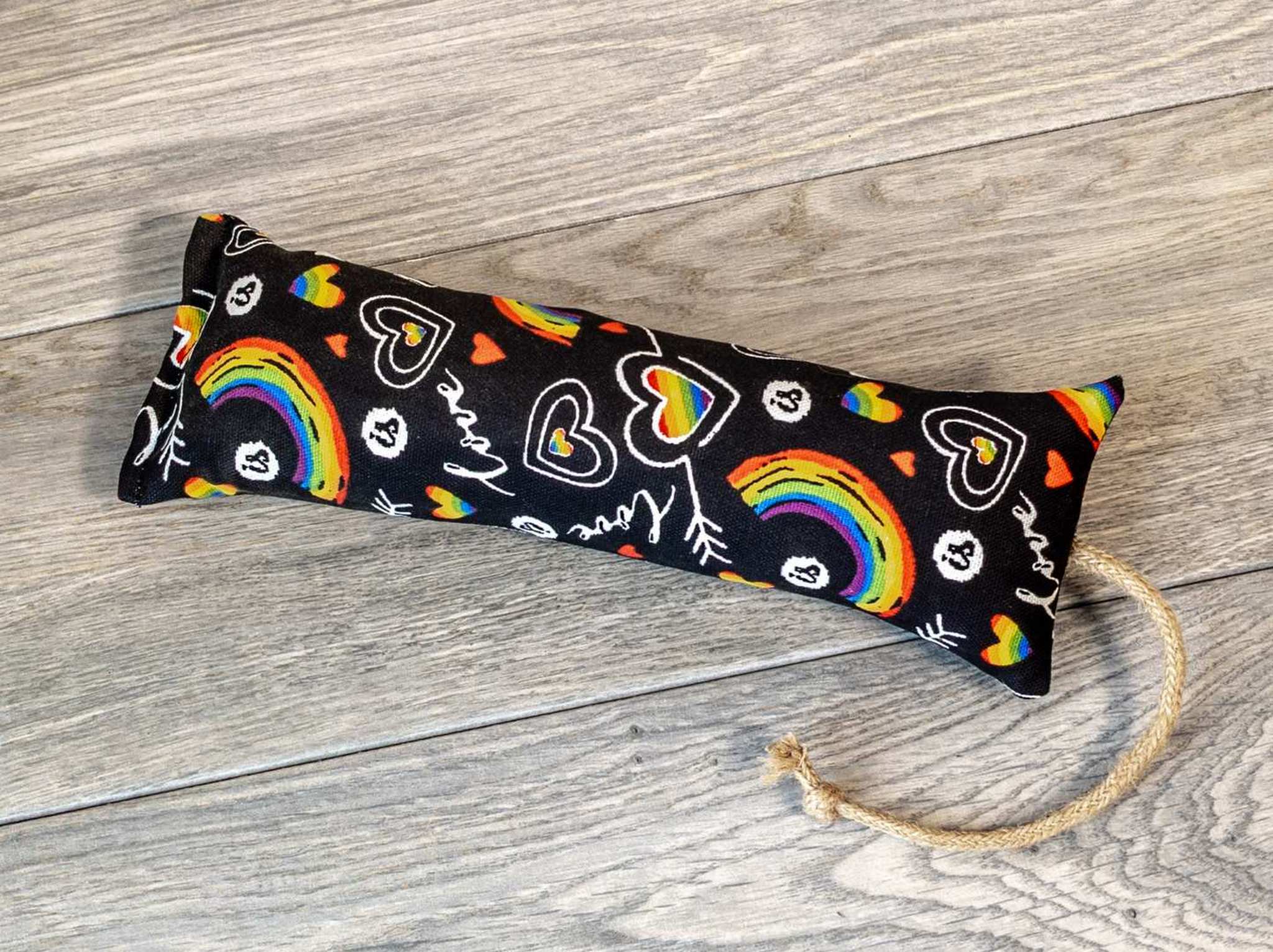 A catnip kicker made from a black fabric that has a pattern of rainbows and the word "love" on it.