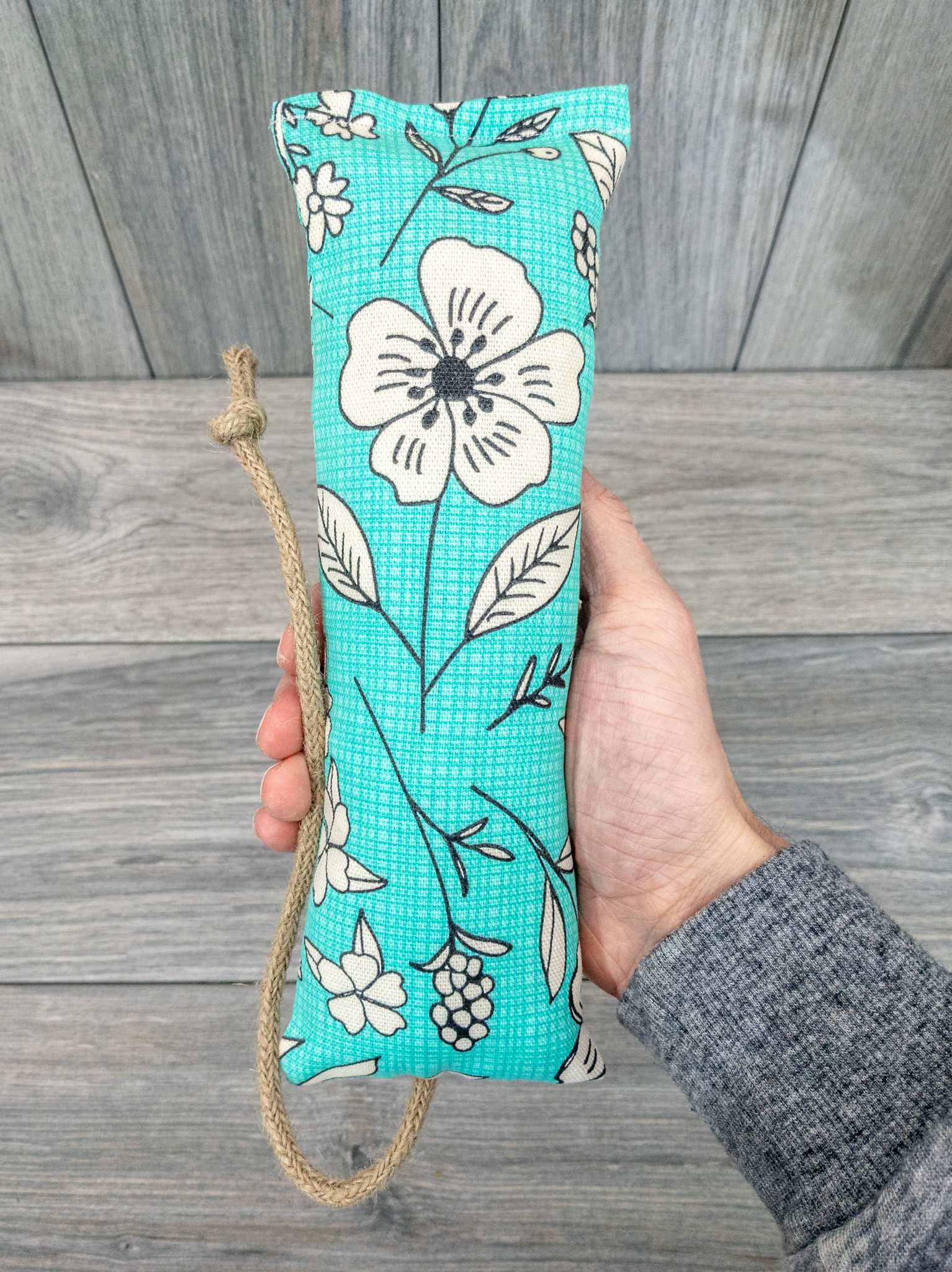 A hand holding a catnip kicker made from a fabric with a green modern pop art flower print