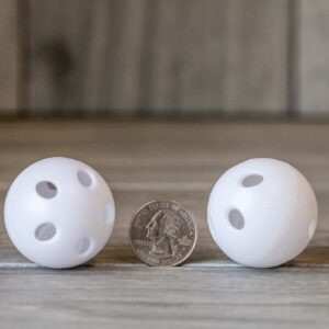White plastic balls with holes and a rattle inside near a quarter for scale
