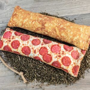 A catnip kicker that looks like pizza with cheese and peperoni on the top half and the crust on the lower half.  It is on top of a pile of catnip