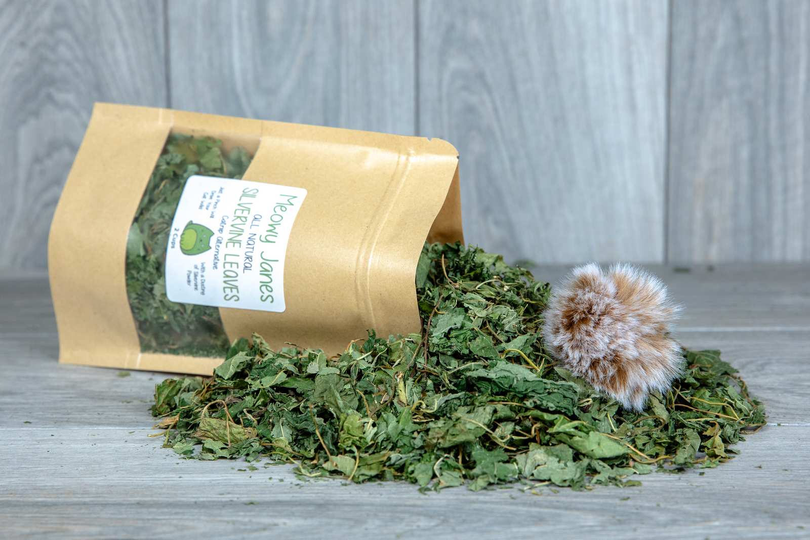 A bag of silvervine leaves with a pile of silvervine leaves pouring out of it with a fuzzy ball toy.