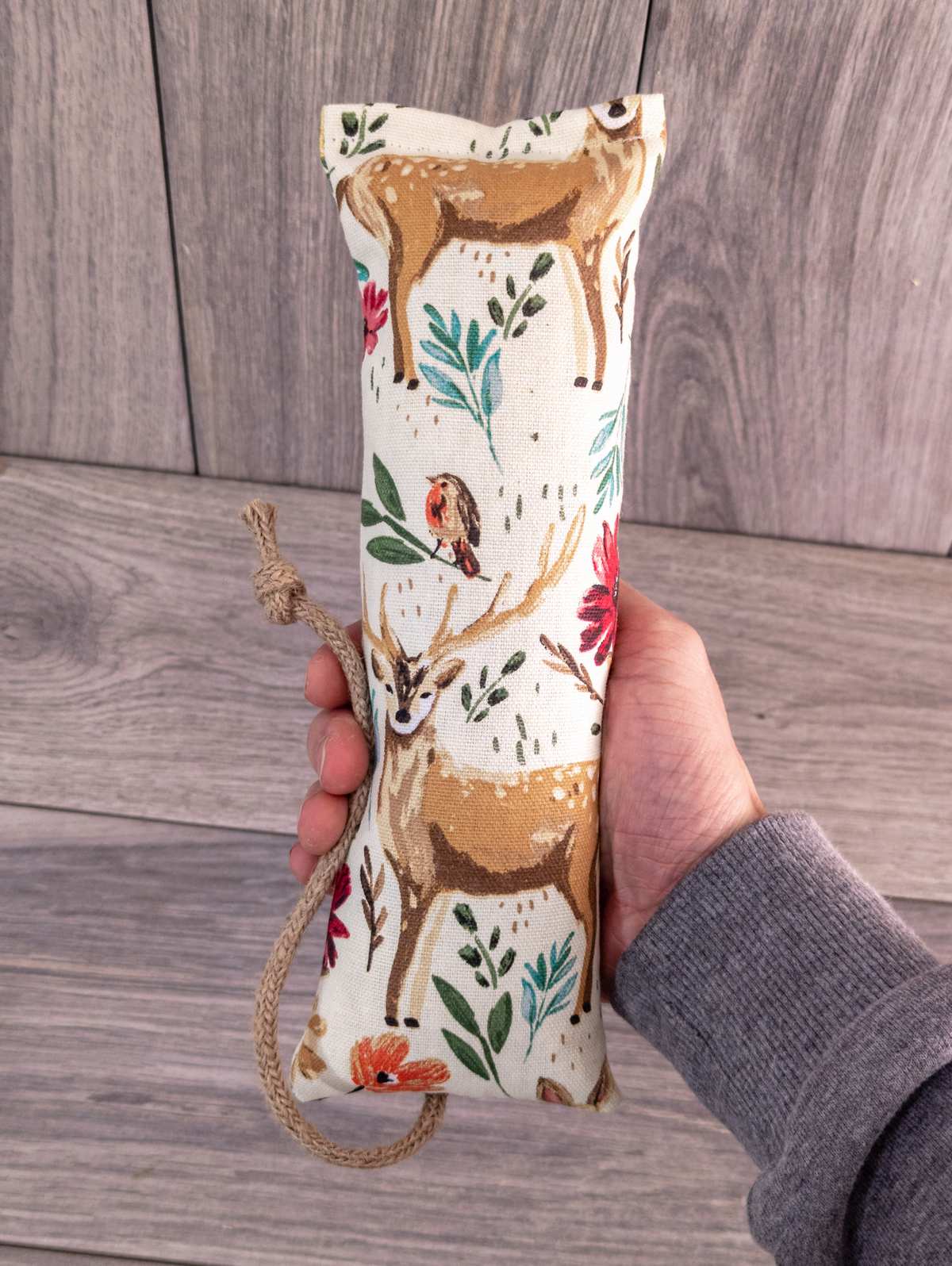 A hand holding a catnip kicker made out of a white woodland themed fabric.