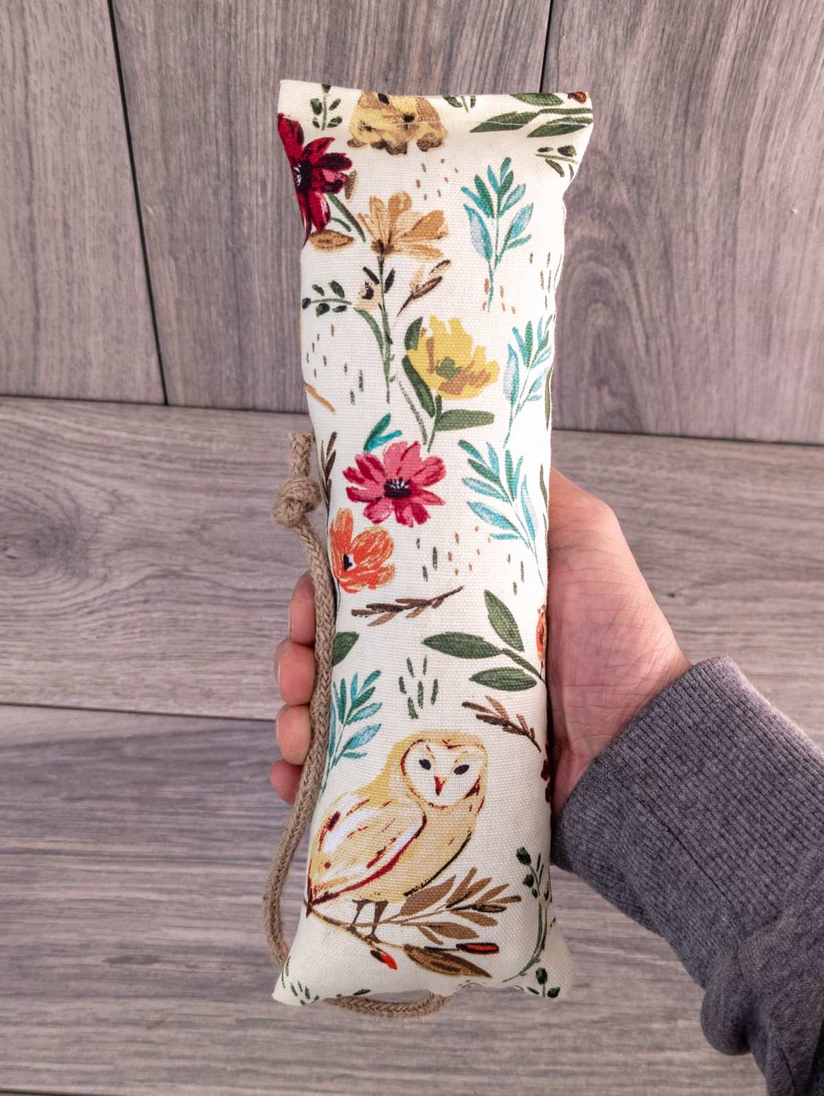 A hand holding a catnip kicker made out of a white woodland themed fabric.