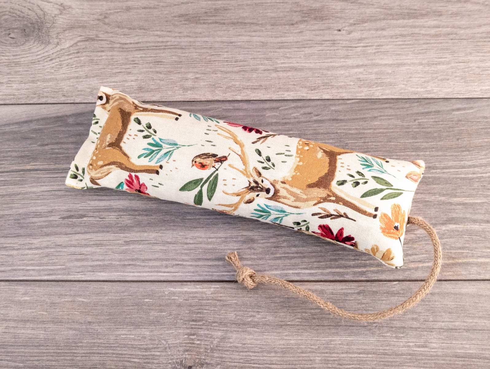 A hand holding a catnip kicker made out of a white woodland themed fabric.