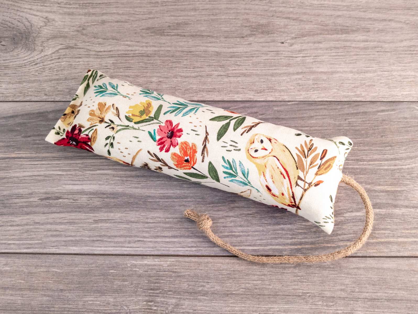 A hand holding a catnip kicker made out of a white woodland themed fabric.