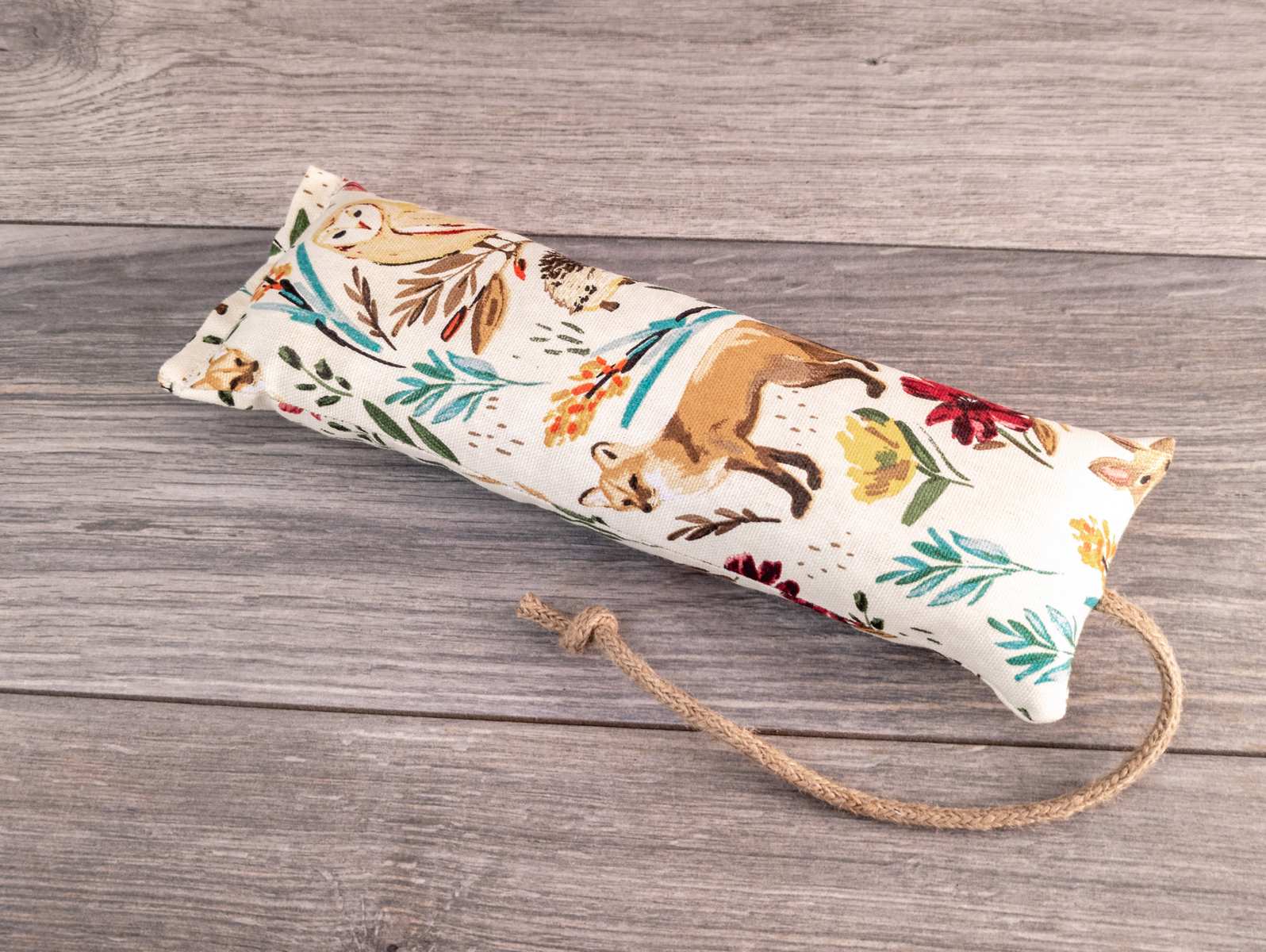 A hand holding a catnip kicker made out of a white woodland themed fabric.
