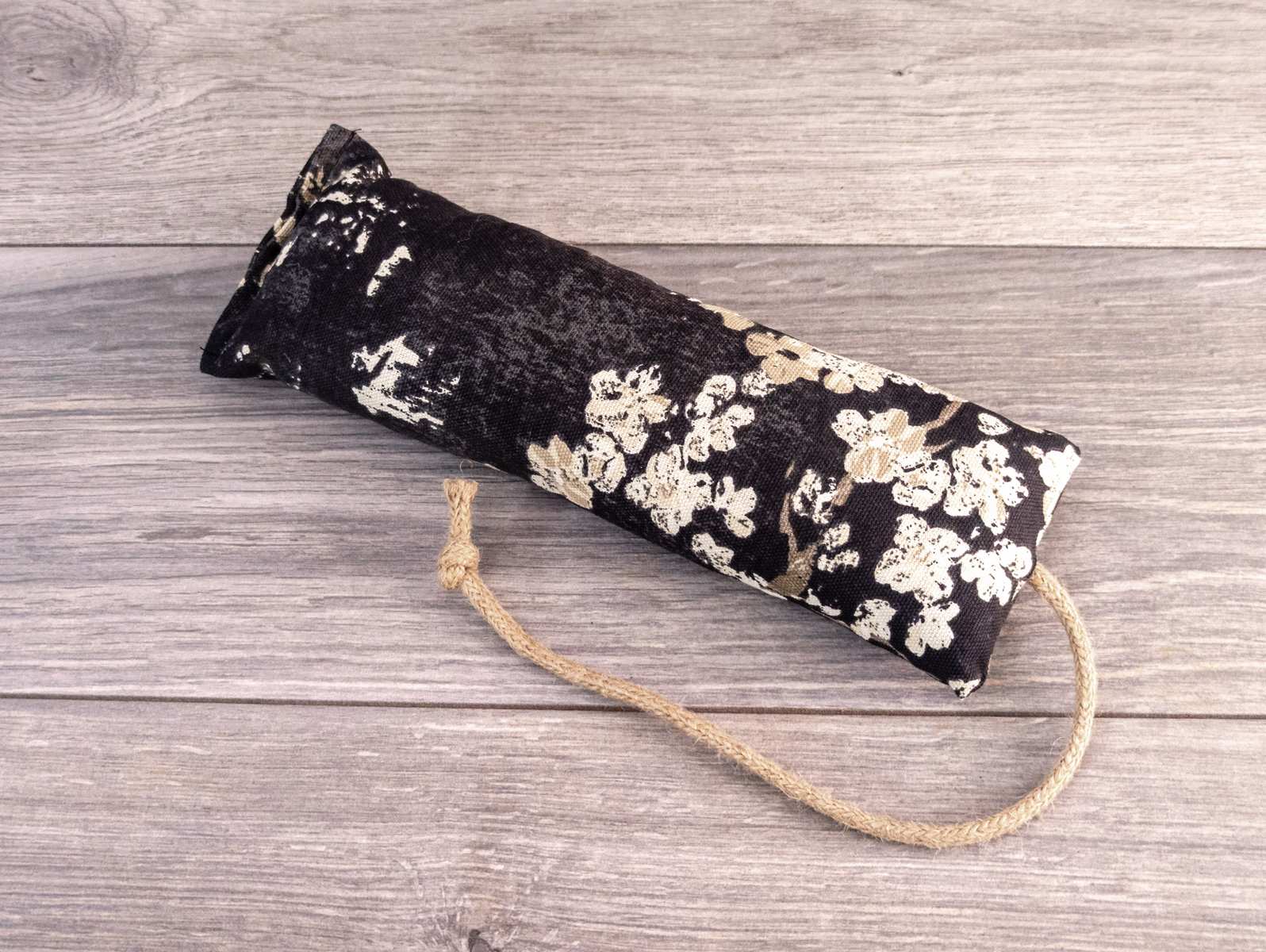 A hand holding a catnip kicker made out of a black cherry blossom themed fabric.