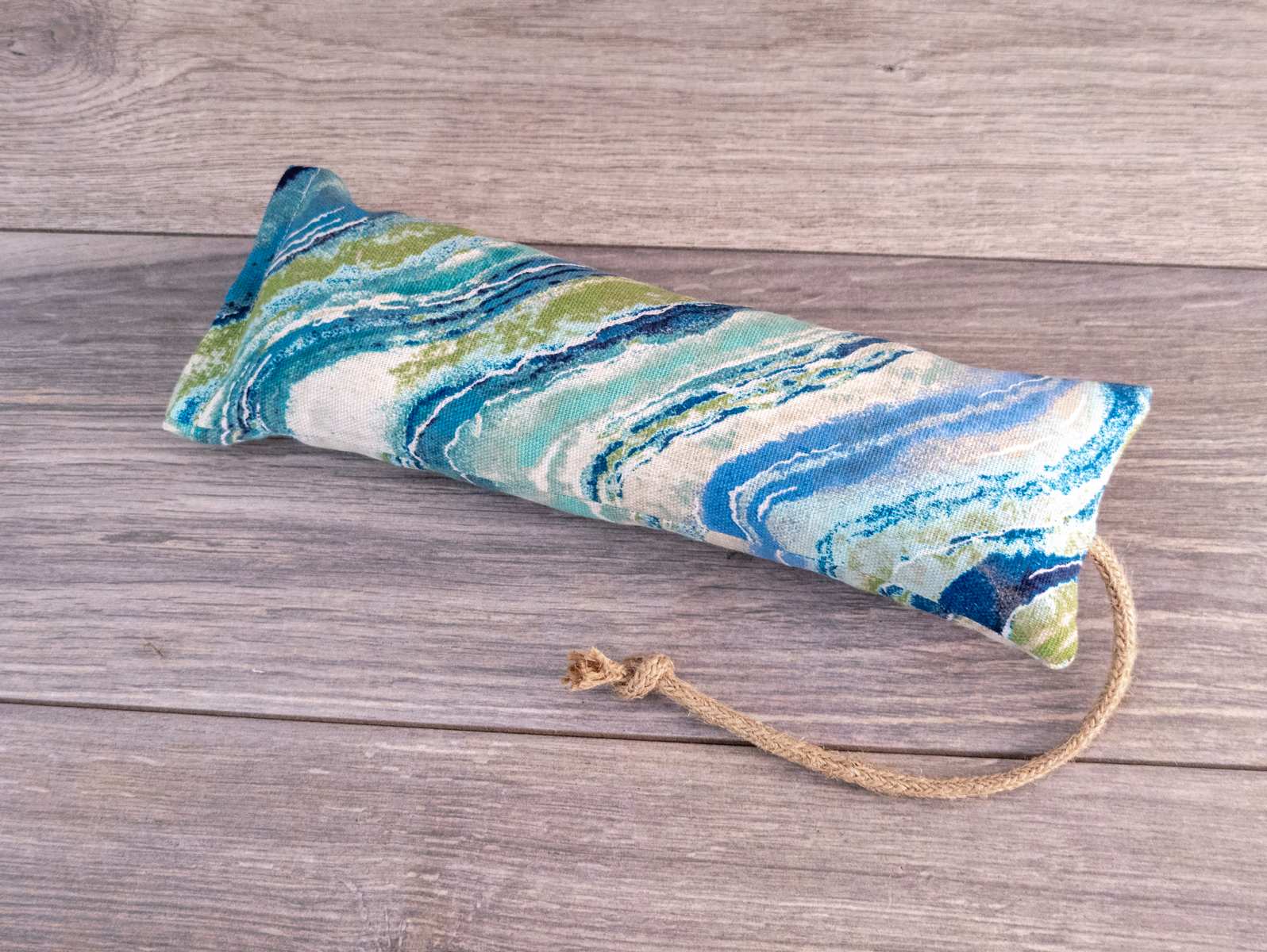 A hand holding a catnip kicker made out of a blue and white natural striped fabric.