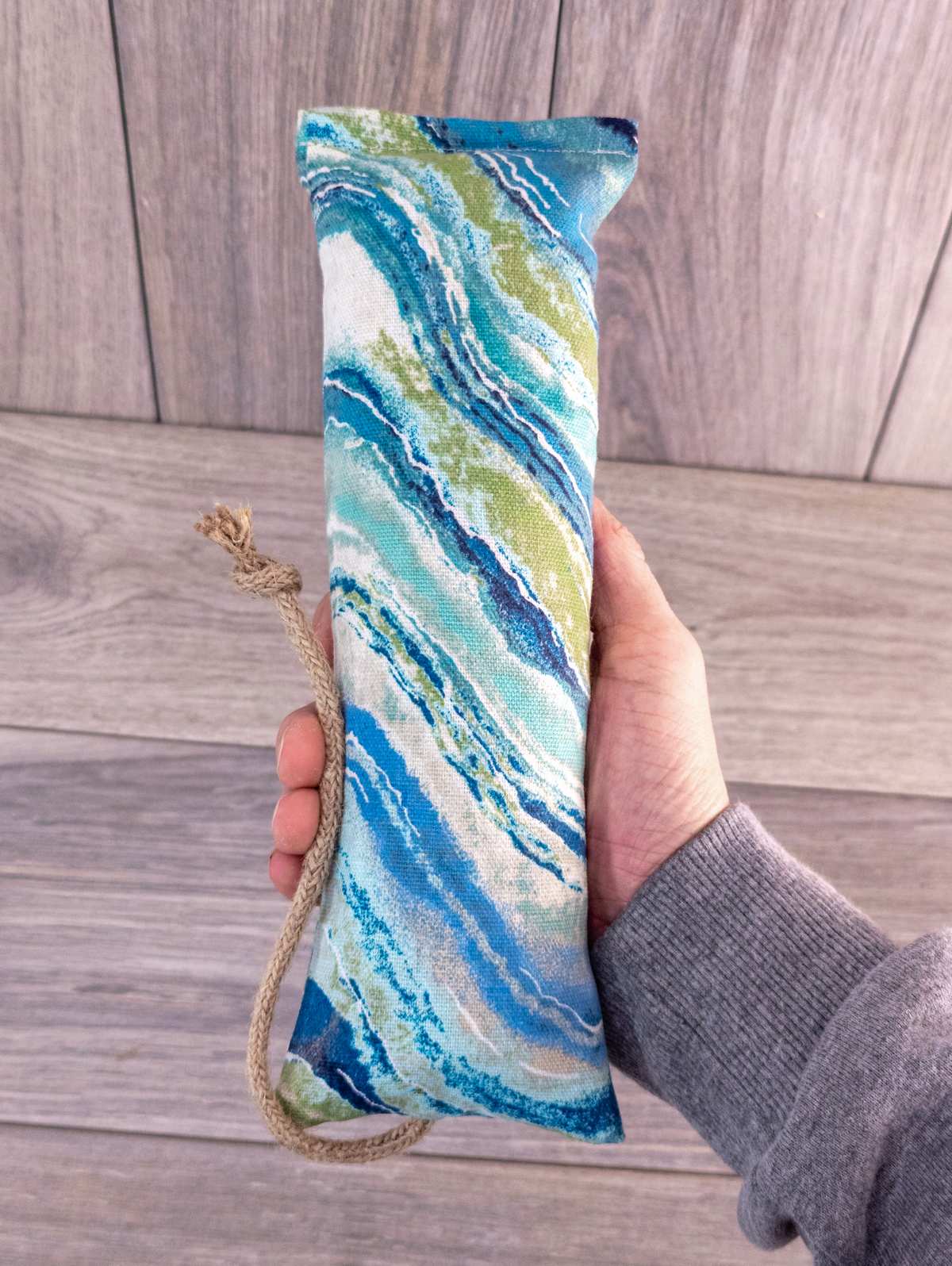 A hand holding a catnip kicker made out of a blue and white natural striped fabric.