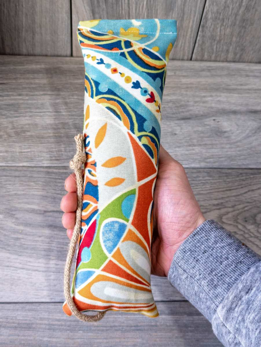 A hand holding catnip kicker cat toy made out of a fabric with a multi color maximalist print