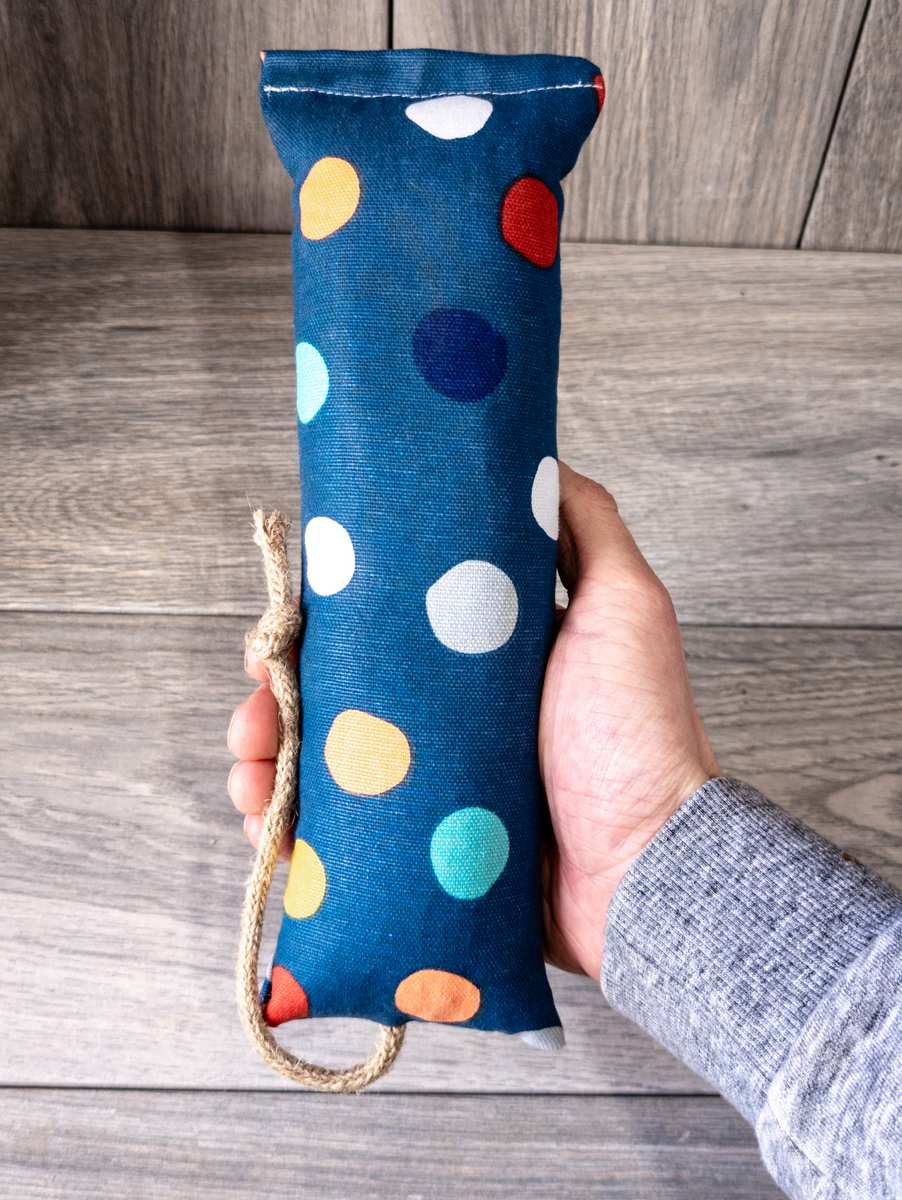 A hand holding a catnip kicker cat toy made out of a fabric with a polka dot print