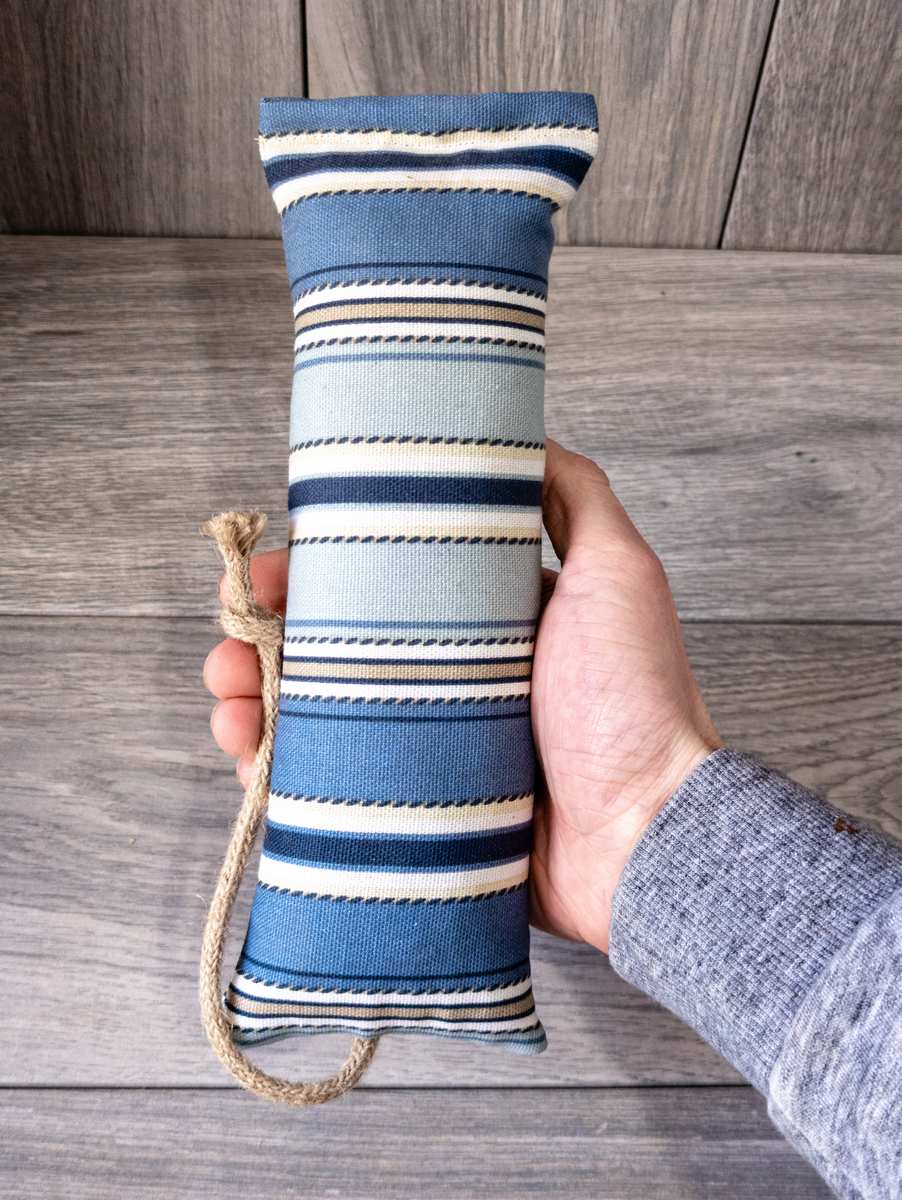 A hand holding a catnip kicker cat toy made out of a fabric with a blue nautical stripe print