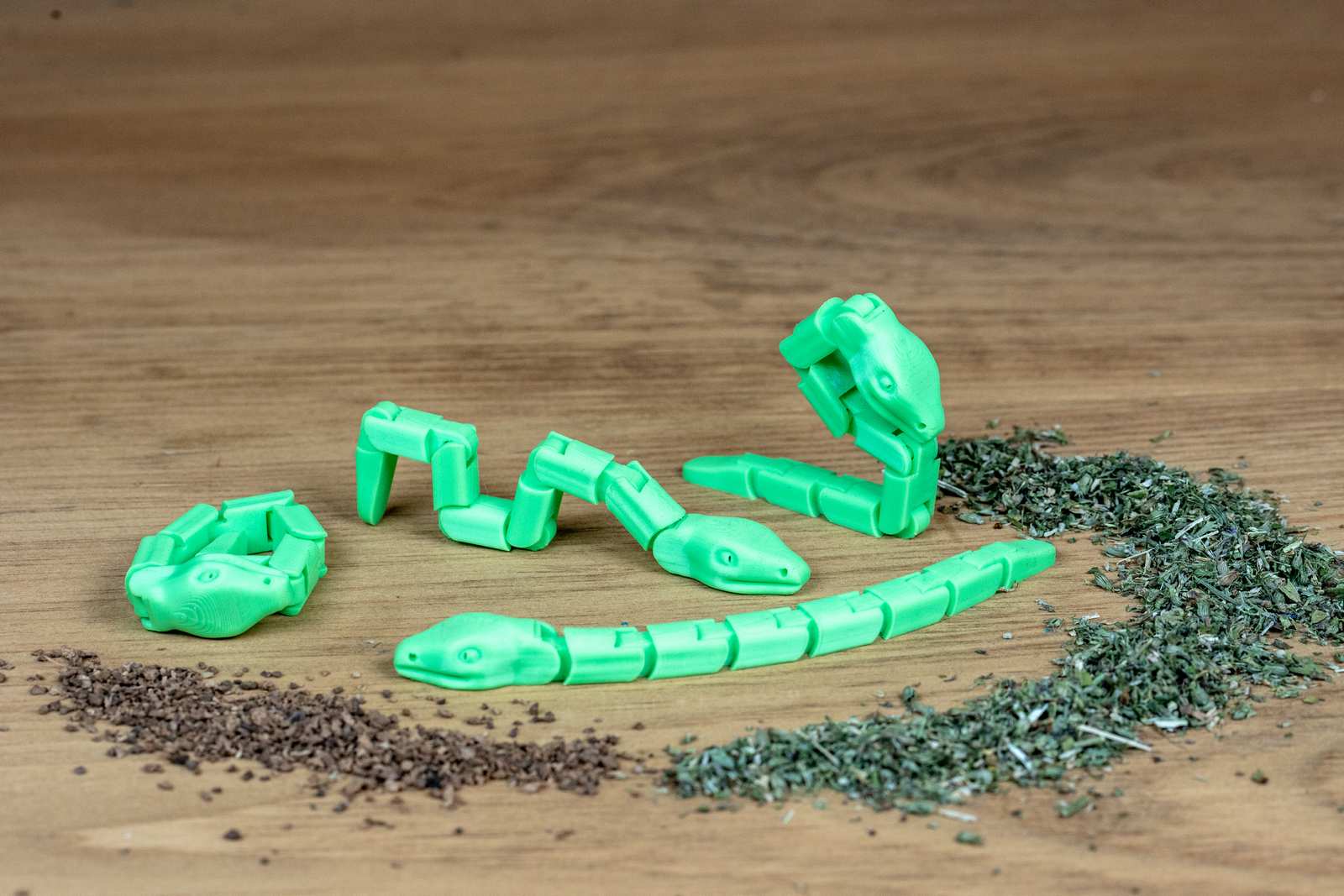 Green articulated snake toys in various positions with piles of catnip and silvervine