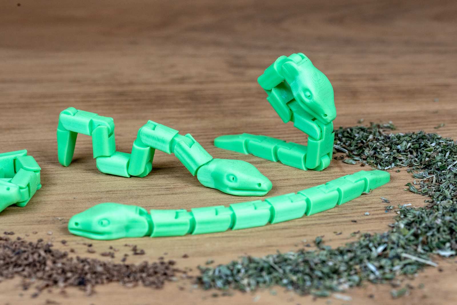 Green articulated snake toys in various positions with piles of catnip and silvervine