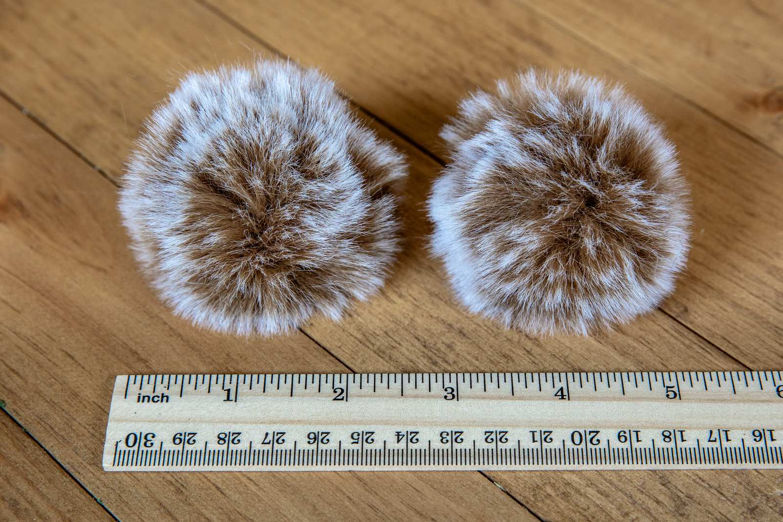 Fuzzy pom pom cat toys next to a ruler showing they are around 2 inches big.