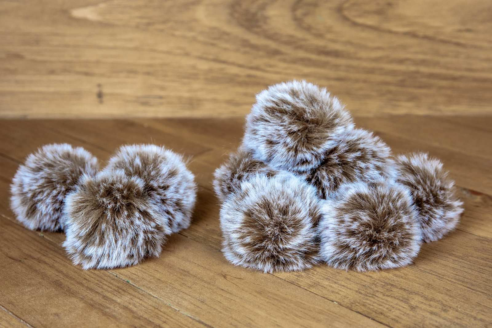 10 grey and brown round cat toys that look like fuzzy pom poms with long hairs.