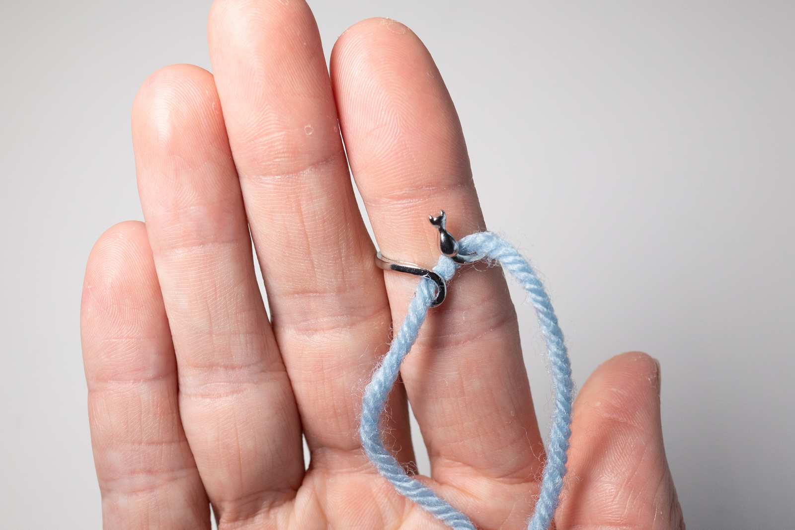 A metal ring that looks like a cat on a persons finger with blue yarn through it.
