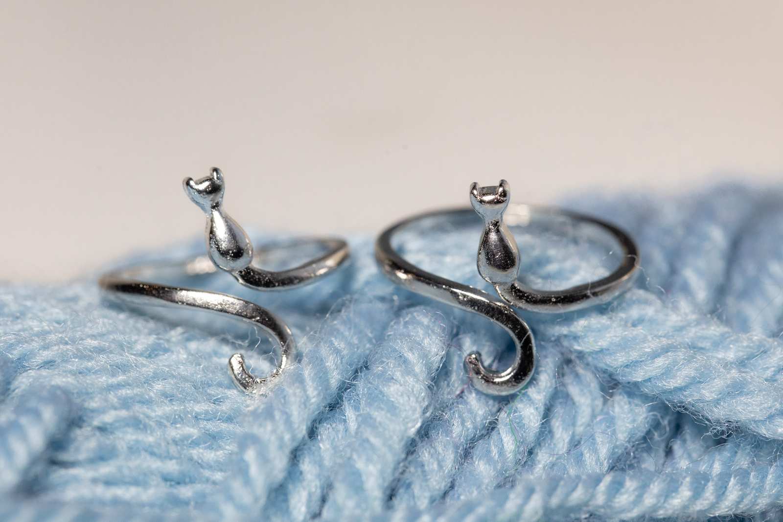 Two metal rings that look like cats on blue yarn