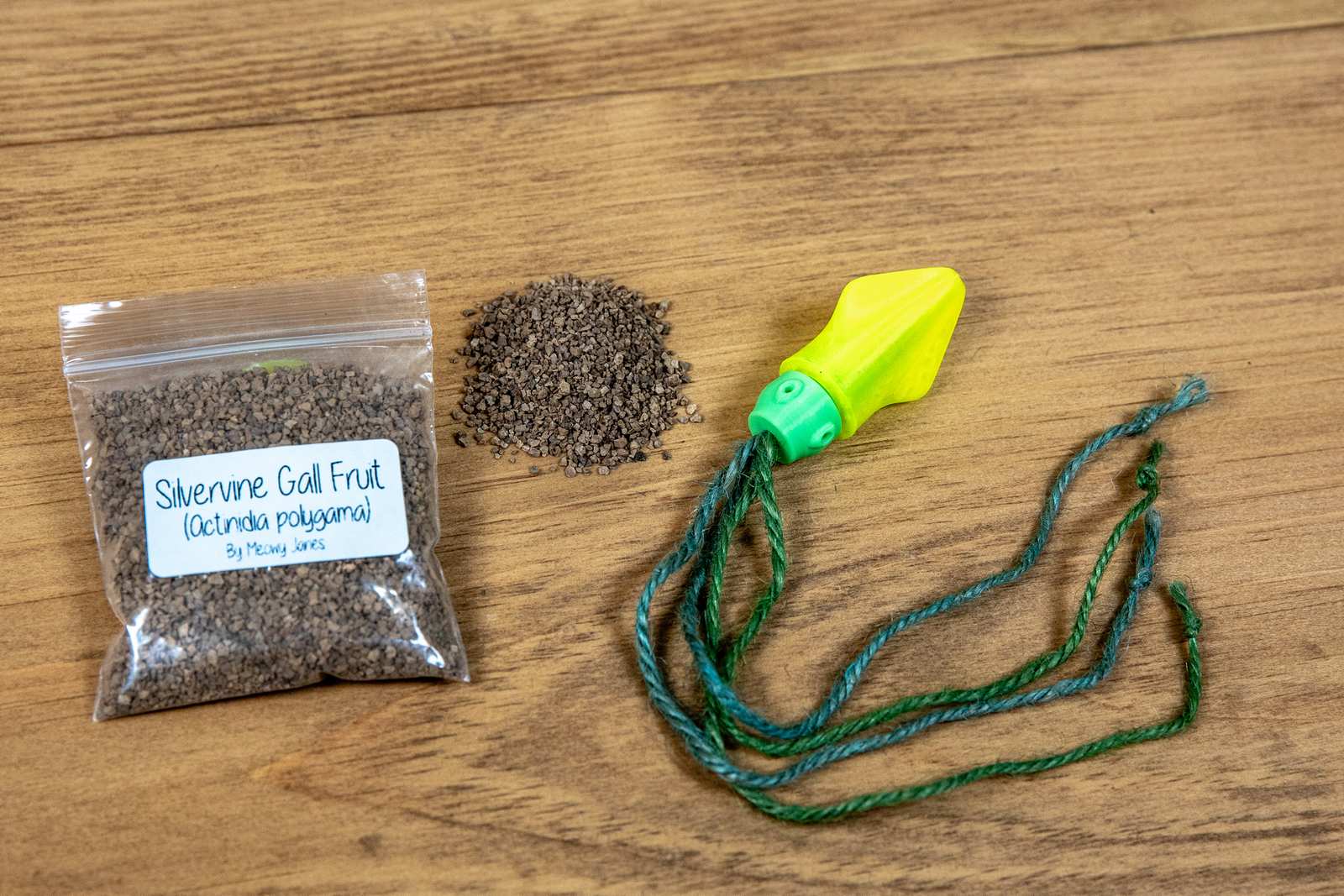 A cat toy that looks like a small squid with yellow body, green head, and jute tentacles. A bag of silvervine is held next to it.