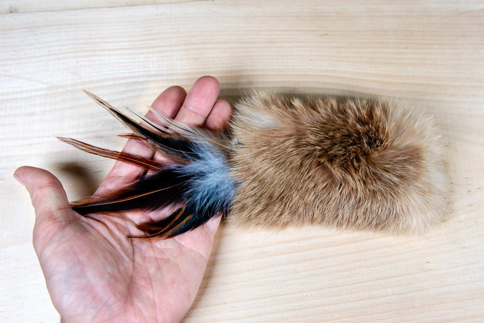 A rectangular cat toy made of rabbit fur and feathers with a human hand for scale