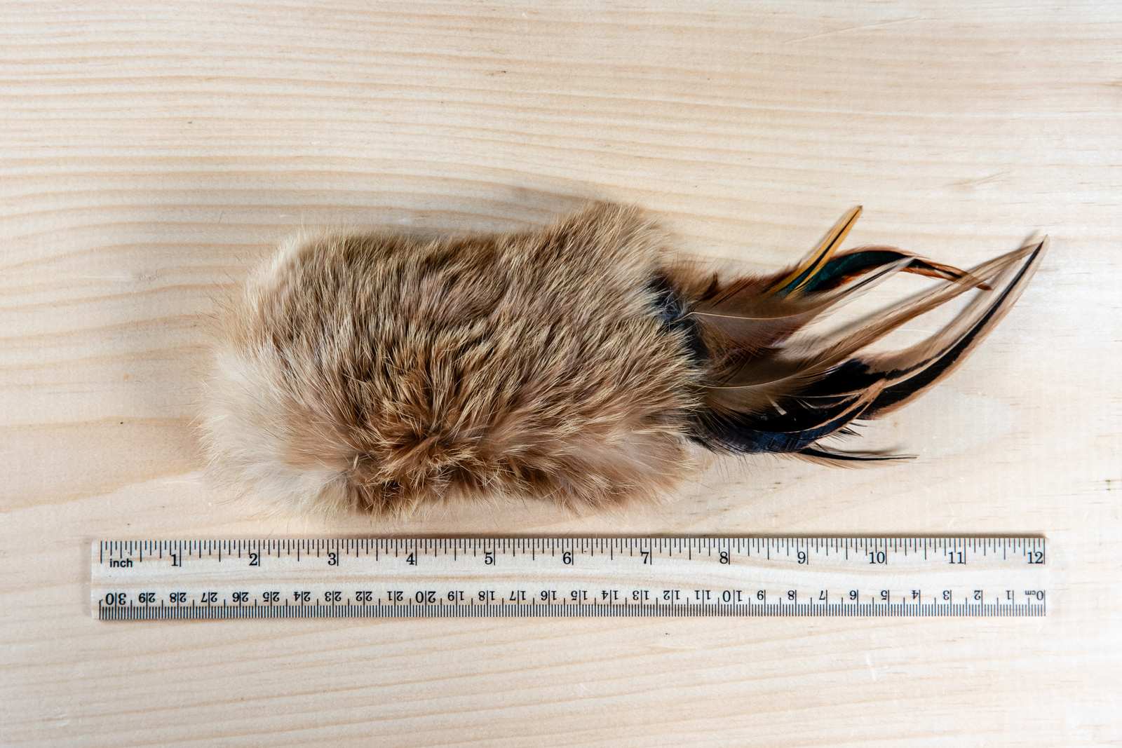 A rectangular cat toy made of rabbit fur and feathers with a ruler for scale