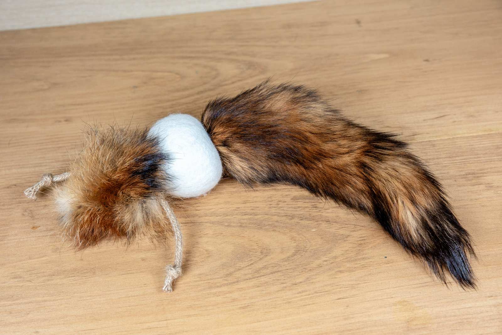 A orange cat toy made out of a fox tail attached to a wool ball