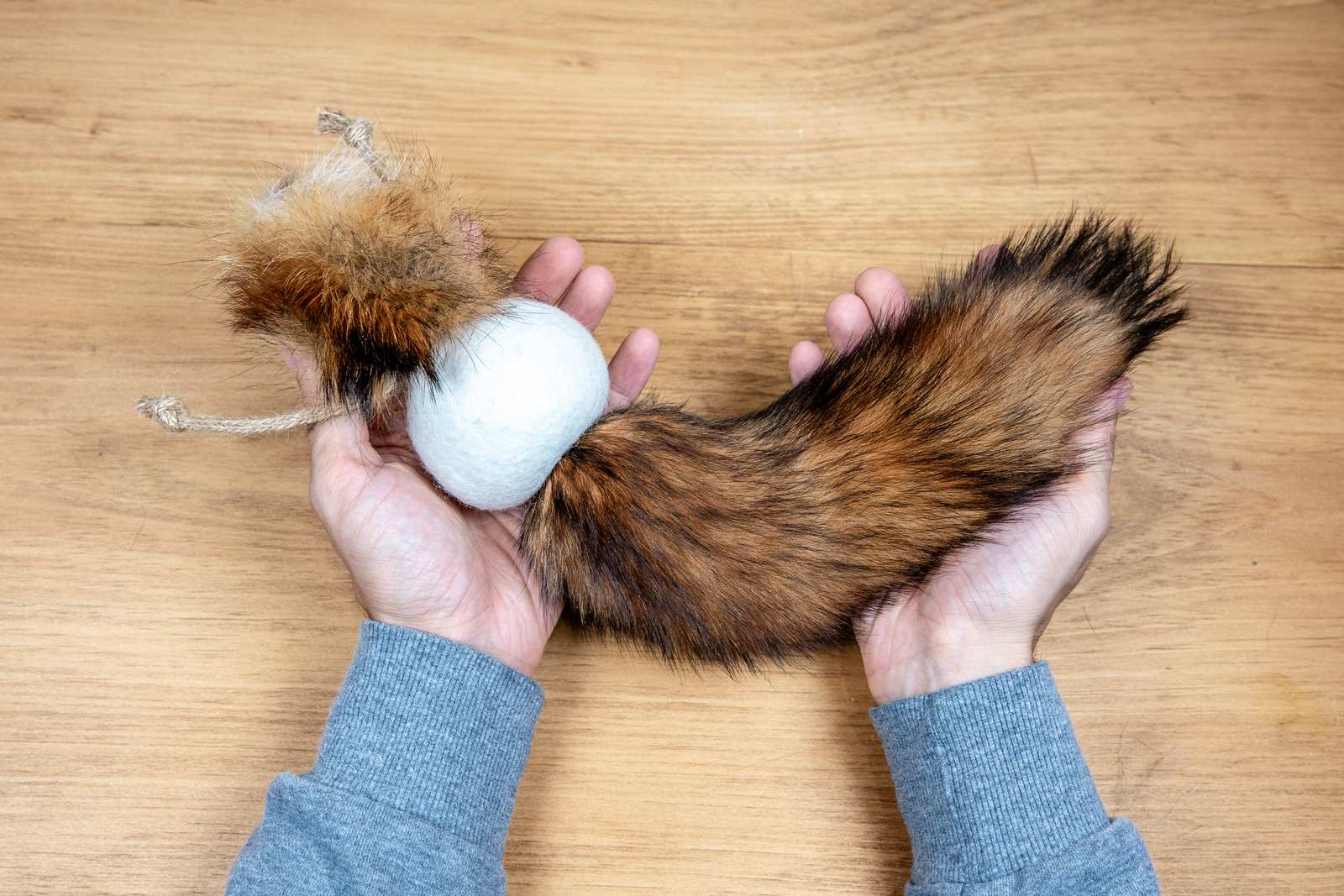 A persons hands holding the orange fox tail cat toy