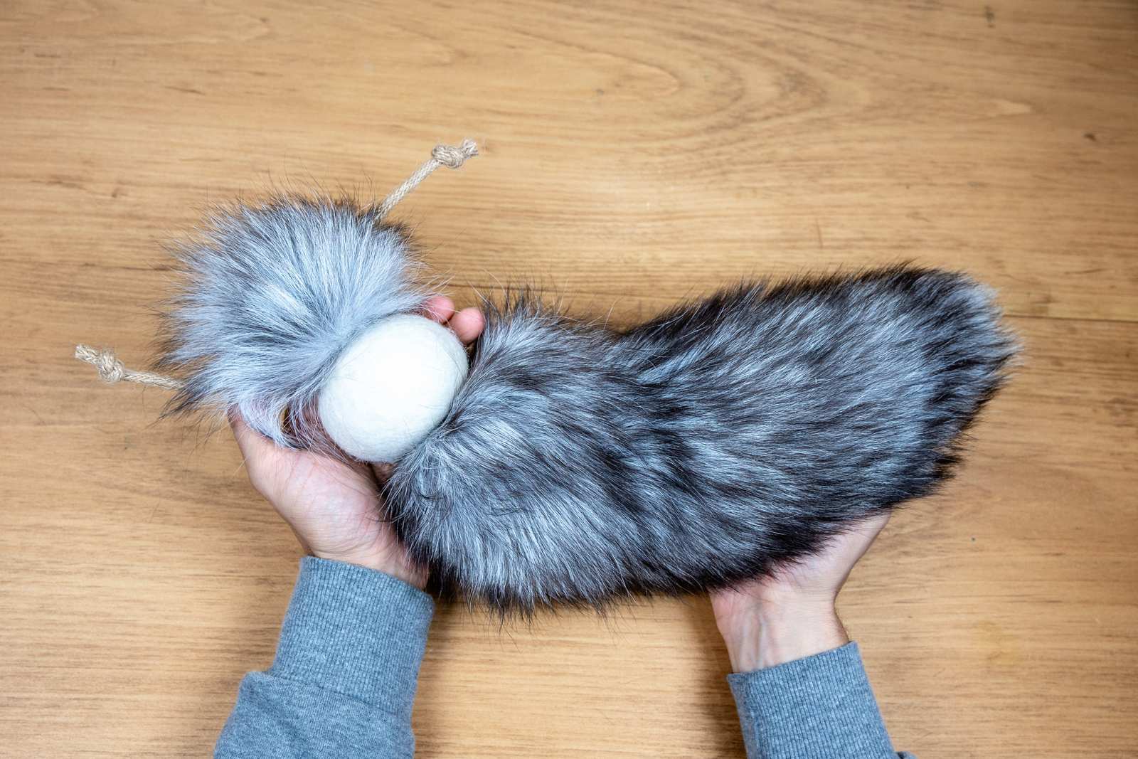 A persons hands holding the grey fox tail cat toy
